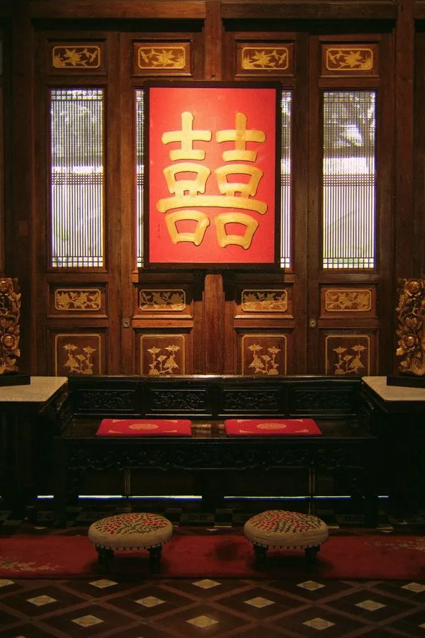 Double happiness sign above a carved wooden bench in a Peranakan mansion, set for a tea ceremony